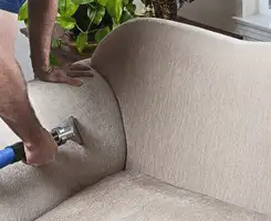 Professional upholstery cleaner deep-cleaning a fabric sofa with a handheld extraction tool and hose in Aurora, CO.